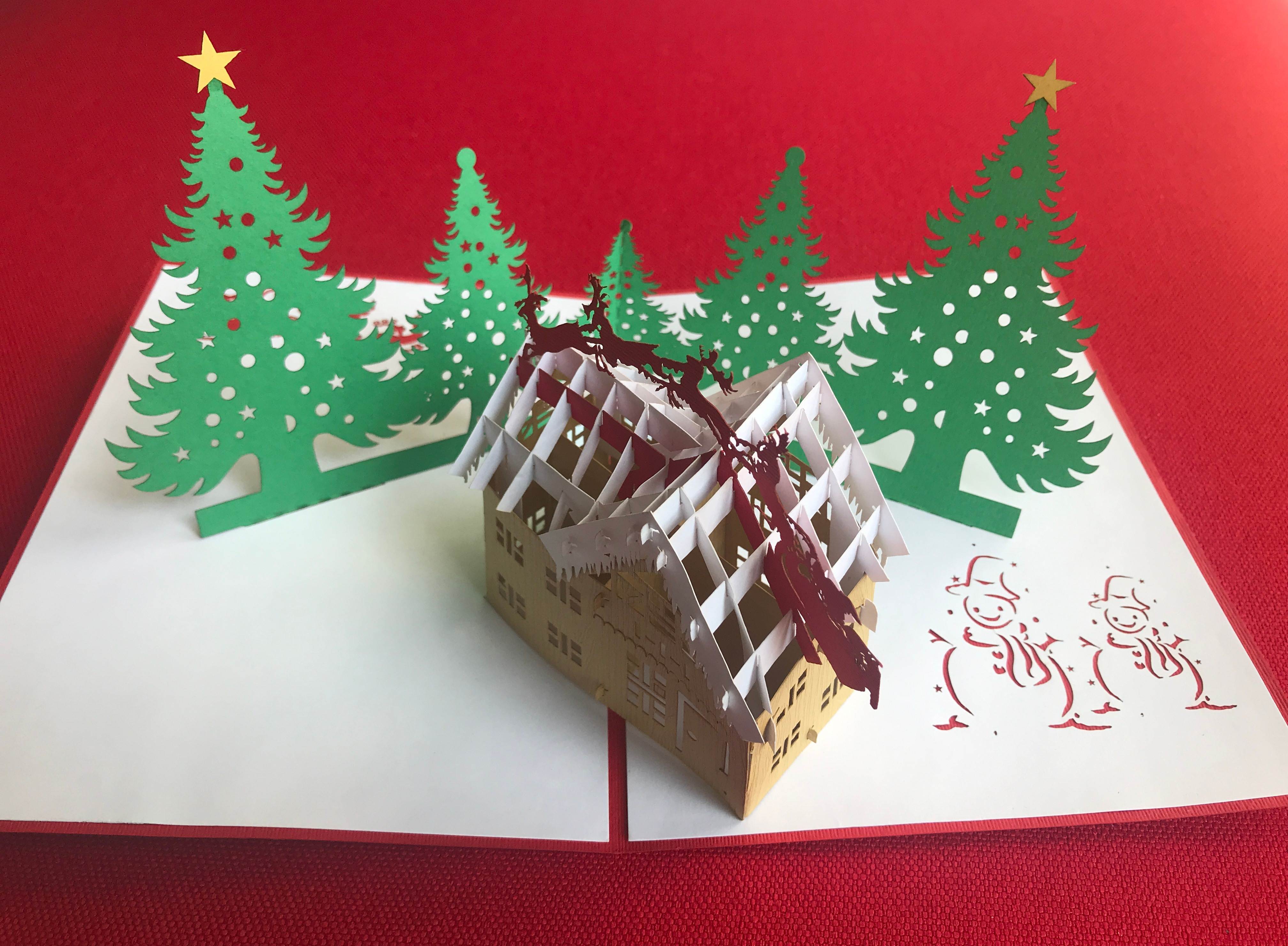 Weihnachtskarte mit Haus, Bäumen und Rentieren